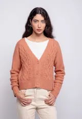 Cardigan de punto color salmón, con diseño de trenzas y diferentes texturas, cierre frontal con botones a tono y cuello en V.