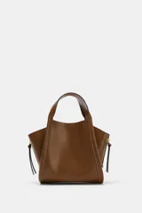 Bolso bandolera de formato city color marrón, con diseño estructurado, pespuntes decorativos, doble asa de mano y cremalleras laterales con tiradores colgantes.