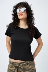 Remera negra de punto acanalado, con cuello redondo, manga corta raglán y ruedo con terminación ondulada.