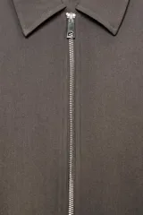 Chaqueta de corte corto y diseño abullonado en color marrón oscuro, con cuello solapa, mangas largas con puños elásticos y cierre frontal con cremallera metálica. Cuenta con bolsillos delanteros de doble vivo.