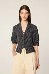 Camisa corta de popelina a rayas con mangas abullonadas, cuello solapa y cierre frontal con botón decorativo. Presenta un diseño con efecto plisado en el pecho y corte ajustado.