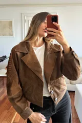 Campera bomber corta de cuero ovino en tono marrón vintage. Presenta solapas clásicas, cierre frontal con botones de guampa y detalles de pasamanería trenzada en las mangas. El interior se encuentra completamente forrado.