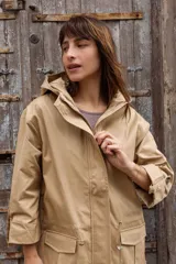 Parka liviana color beige con capucha, cierre frontal con botones, bolsillos delanteros con tapa y ajuste en la cintura. Presenta mangas con puños vueltos y detalle de botones.