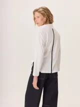 Remera blanca de manga larga con cuello alto, corte holgado y detalle de una tira vertical negra con inscripción dorada en la espalda.