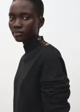 Vestido corto de punto negro con cuello alto y detalle de botones metálicos en el hombro.