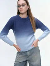 Buzo tejido de punto con diseño degradé que transiciona de azul oscuro a celeste claro. Presenta cuello redondo, mangas largas y puños acanalados, con un corte holgado y relajado.