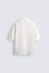 Camisa de corte relajado confeccionada en tejido fluido con mezcla de viscosa, color negro. Presenta cuello solapa, manga corta, cierre frontal con botones y un bordado a contraste en el pecho.
