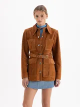 Parka de gamuza color ocre con diseño de estilo safari, cuello camisero, cierre frontal con broches metálicos, múltiples bolsillos frontales y cinturón ajustable con hebilla metálica.