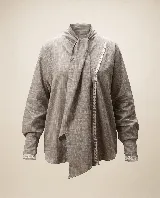 Camisa gris de algodón con textura sutil, corte relajado y mangas amplias. Cuenta con cuello mao con lazo largo para anudar, y detalles de puntilla blanca a contratono en la parte delantera y en los puños.