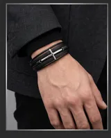 Pulsera multicapa de cuero negro con diseño trenzado y dije central de cruz en acero inoxidable.