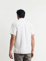 Camisa de manga corta a rayas verticales color natural y celeste, con cuello clásico, cierre frontal con botones de madera y bolsillo de parche en el pecho.