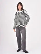 Buzo de punto a rayas horizontales blancas y negras, con cuello camisero blanco con volados y cierre frontal de botones.