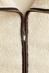 Campera de corte holgado confeccionada en tejido de sherpa suave, con cuello alto y cierre frontal. Presenta detalles de ribetes en contraste y diseño de hombros caídos.