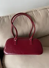 Cartera de mano tipo bowling color bordó, confeccionada en material sintético con textura arrugada. Cuenta con doble asa fija y cierre superior.