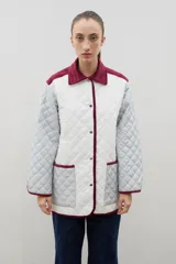 Campera acolchada de diseño patchwork con paneles en color blanco y gris claro. Presenta cuello camisero y ribetes en color bordó, cierre frontal con botones metálicos y dos bolsillos delanteros aplicados.