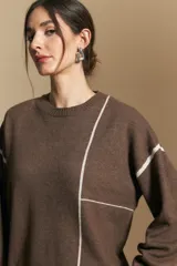 Sweater de punto color marrón con diseño de líneas blancas en contraste. Presenta cuello redondo, mangas largas y puños tejidos, con una estética minimalista y moderna.