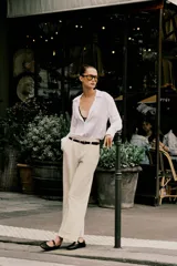 Pantalón de vestir color beige, tiro alto, corte ancho y pierna recta. Presenta un bajo con vuelta y viene acompañado de un cinturón fino de cuero marrón con hebilla metálica.