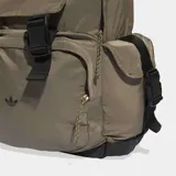 Mochila Adidas de diseño utilitario en color marrón, con compartimento principal amplio, bolsillo frontal con solapa y hebillas ajustables, y bolsillos laterales con solapa. Presenta el logo del trébol en la parte inferior frontal y detalles en negro.