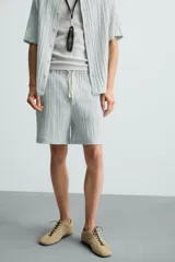 Bermuda negra de corte regular, confeccionada en tejido jacquard con efecto arrugado. Presenta cintura elástica ajustable con cordón blanco, bolsillos laterales y bolsillos traseros de vivo.