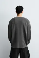 Camiseta de manga larga con cuello redondo, confeccionada en tejido de algodón con textura tipo waffle y efecto lavado. Presenta un corte relajado con puños en rib y bajo irregular.