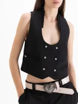 Chaleco Capri de corte cropped y calce al cuerpo, confeccionado en tejido color negro. Presenta escote redondo pronunciado con detalle de volados tableados que recorren el contorno y cierre cruzado delantero con seis botones metálicos. Incluye bolsillos frontales ojal.