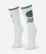 Medias de caña larga color blanco con detalles en verde, que incluyen un estampado de carita sonriente y el texto 'Smile Origins' en el lateral. Cuentan con franjas verdes en el borde superior.