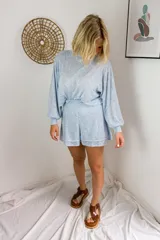 Conjunto de dos piezas en color crema, compuesto por un buzo de cuello alto, mangas largas abullonadas y ajuste en la cintura, junto con un short de tiro alto con terminaciones al corte.