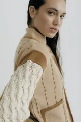 Chaqueta de punto con diseño color block en negro, beige y marrón. Presenta cuello redondo, cierre frontal con botones grandes, bolsillos frontales y detalles de costuras decorativas verticales en color claro.