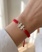 Pulsera de hilo rojo trenzado en macramé, con dije central de plata 925 con diseño de dos nenas tomadas de la mano y cierre regulable.