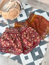 Short de seda con elástico fruncido en la cintura y volado en el ruedo. Presenta un estampado vibrante en tonos rojo/bordó y turquesa con motivos florales o arabescos.