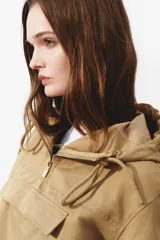 Campera popover color tostado confeccionada en sarga de mezcla de algodón y lyocell. Cuenta con capucha con cordón ajustable, medio cierre frontal y un amplio bolsillo delantero con solapa. Presenta diseño de hombros caídos, canesú frontal, mangas abullonadas con pliegues, puños con cierre ajustable de botón y bajo con cordón interior para fruncir.