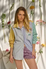 Camisa de manga larga con diseño patchwork de rayas en tonos verde, lila, amarillo y azul. Cuenta con cuello camisero, cierre frontal con botones y un bolsillo en el pecho con el logotipo bordado "pur".