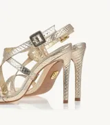 Sandalias de tacón alto color dorado con textura de piel de serpiente, tiras cruzadas en el empeine y pulsera con hebilla en el tobillo.