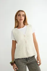 Chaleco de punto con escote en V y cierre frontal de botones. Presenta un diseño de corte recto y textura jaspeada en tono crema.