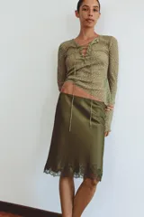 Camisa semitransparente color verde militar con tejido jacquard, escote en pico con cordones cruzados y lazada frontal, y mangas largas acampanadas.