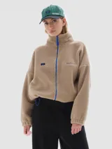 Campera de sherpa color beige con cuello alto, cierre frontal completo en color azul a contratono y bordado en el pecho.