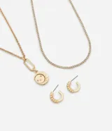 Conjunto de bisutería compuesto por dos collares y un par de aros tipo argolla. El primer collar es una cadena estilo riviere con strass, y el segundo collar presenta una cadena con un dije circular con diseño de luna y estrellas. Los aros son argollas pequeñas con detalle de relieve.