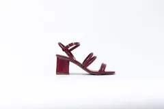 Sandalias de tacón cuadrado medio, confeccionadas en charol rojo. Presentan un diseño de tiras tubulares sobre el empeine y cierre con pulsera ajustable al tobillo mediante hebilla metálica.
