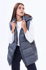 Chaleco puffer largo de color negro, con cierre frontal completo, capucha ajustable con cordones y bolsillos laterales. Diseño acolchado con costuras horizontales.