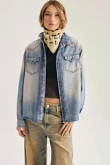 Camisa de denim azul con lavado gastado, bolsillos con solapa en el pecho, cuello en punta y cierre frontal de broches metálicos.