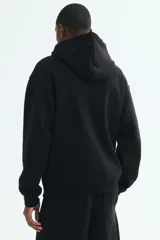 Canguro de corte holgado en mezcla de algodón, de color negro, con hombros caídos, capucha con cordón ajustable, bolsillo frontal tipo canguro y terminaciones en rib acanalado en puños y cintura.