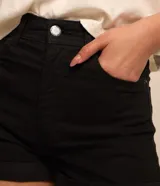 Short de sarga color blanco, de cintura alta, con bolsillos delanteros y traseros, trabillas para cinturón y bajo plegado. Cuenta con cierre frontal de botón y cremallera.