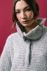 Buzo tejido en mohair de color gris, con silueta amplia y corte en línea A. Presenta cuello tipo remera con broches que permiten cerrarlo como polera, mangas largas con puños y un diseño de tejido horizontal.