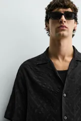 Camisa de corte relajado con cuello bowling y manga corta. Confeccionada en tejido fluido con textura jacquard de patrón geométrico y cierre frontal de botones.