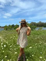 Vestido corto de lino con estampado floral en tonos rojizos y verdes sobre base clara. Presenta volados en las mangas y cierre posterior con botones forrados en la misma tela.