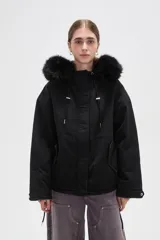 Campera negra de algodón con capucha, cierre frontal oculto y bolsillos laterales. Presenta un diseño holgado con detalles de piel sintética en el borde de la capucha.