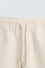Bermuda de algodón color beige claro, de corte regular fit, con cintura elástica ajustable mediante cordón. Presenta bolsillos laterales y un bolsillo trasero de vivo.