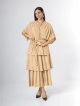 Vestido midi de crepé color beige, con escote en V cruzado, mangas cortas amplias, cintura elastizada con lazo ajustable y falda de múltiples niveles con volados.