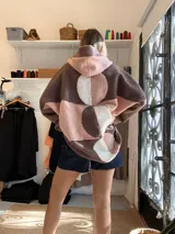 Campera tipo hoodie confeccionada en tejido de corderito sintético con diseño de bloques geométricos en tonos marrón, rosado y blanco. Presenta capucha amplia, corte oversize y mangas largas.