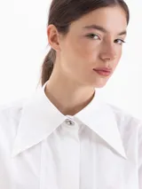 Camisa de poplín de algodón con corte holgado y largo hasta la cadera. Presenta cuello clásico con detalle de herraje metálico, cartera oculta con botones al tono y puños anchos con botones.